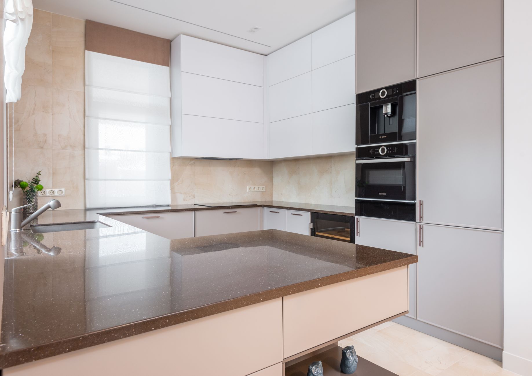 Contemporary kitchen with white and beige cupboards and built in appliances and cutting table laid with in Riverside, CA